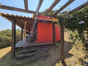 a house with a wooden porch with a red wall at Chalés Vila Real - Tranquilidade na Serra de Carrancas - Piscina com uma vista espetacular do Pôr do Sol in Carrancas