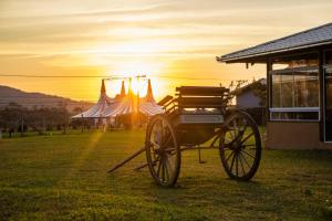 a horse drawn carriage in a field with a sunset in the background at Villa Park Chalés - A sua fazendinha ao lado do Beto Carrero in Penha