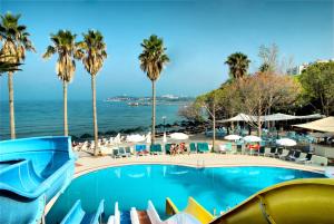a swimming pool with palm trees and the ocean at Ephesia Holiday Beach Club in Kuşadası