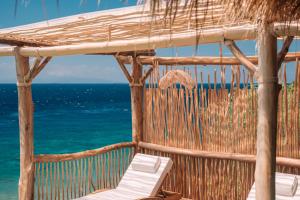 a porch with a straw umbrella and chairs and the ocean at Abing Villas Spa & Beach Bar in Amed
