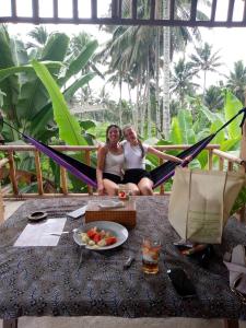テテバトゥにあるSyaqila Homestay Lombokの果物のボウルを持ってハンモックに座っている2人の女性
