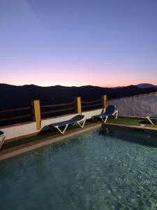 een zwembad met 2 ligstoelen naast het water bij Casa Villazo II in Almáchar