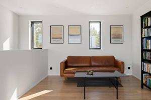 a living room with a brown couch and a book shelf at Exklusiv villa med pool & fri havsutsikt in Sommarbo