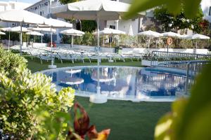 a swimming pool with white chairs and umbrellas at Coral Compostela Beach Golf in Playa de las Americas