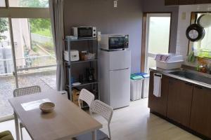a kitchen with a table and a refrigerator with a microwave at ペットと泊まれる一棟貸し 海の駅九十九里まで徒歩15分 はうす41マイルズ in Katakai