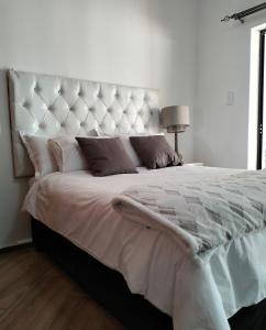 a white bedroom with a large bed with a large headboard at Rest Inn C Guesthouse - 10min from OR Tambo Airport in Boksburg