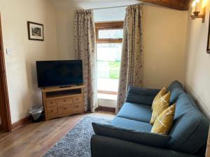 a living room with a blue couch and a television at Tupenny Cottage, Old Mill Farm, Cotswold Water Park in Cirencester