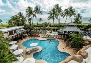 a pool at a resort with palm trees and the ocean at Alexander 1209 Beachfront condo with 2 pools , beach access, sauna, stores in Miami Beach