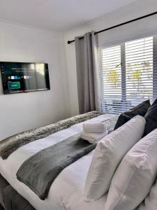 a large bed in a bedroom with a television on the wall at West Beach Luxury Apartment in Bloubergstrand +32 photos