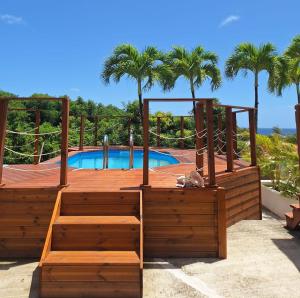 eine Holzterrasse neben einem Pool mit Palmen in der Unterkunft La Canopée - Appartement F2 avec piscine - vue mer in Le Robert + 6 Fotos