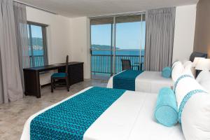 アカプルコにあるRitz Acapulco All Inclusiveのベッド2台、デスク、バルコニーが備わる客室です。