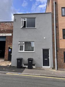 Ein graues Gebäude mit zwei Mülltonnen davor. in der Unterkunft Haven Homes - Central Luton Studio Apartments in Luton