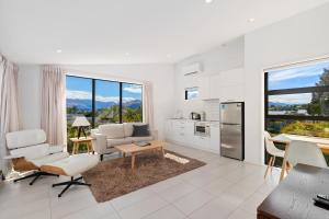 Una sala de estar con muebles blancos y grandes ventanales. en Tenby Apartments, en Wanaka