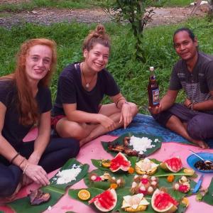 a group of people sitting on a picnic blanket with food at Batu Ridi Jungle in Timbanglawang