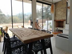 a dining table and chairs in a living room with windows at Prana Cabaña Kira 3 hab in Samaipata