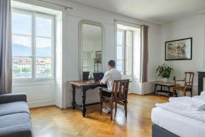 a man sitting at a desk with a laptop in a living room at Vevey Hotel & Guesthouse in Vevey