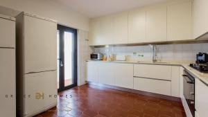 a kitchen with white cabinets and a red tile floor at Greice Homes-650 meters from the beach, 4 bedrooms villa for holidays in Vilamoura-Quarteira in Quarteira