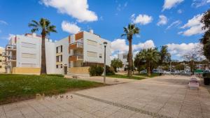 a white apartment building with palm trees and a sidewalk at GREICE HOMES 1 BEDROOM APARTMENT CENTRE OF VILAMOURA in Vilamoura