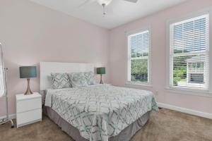 a white bedroom with a bed and two windows at Pelican Pleasure by Sea Scape Properties in Carolina Beach