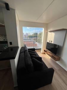 a living room with a black couch and a large window at Apt próximo do metrô carrão in Sao Paulo