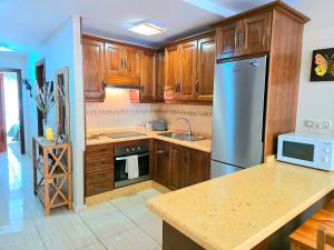 Una cocina con gabinetes de madera y un refrigerador de acero inoxidable. en Hada Coast Apartment Playa San Juan, en Playa de San Juan