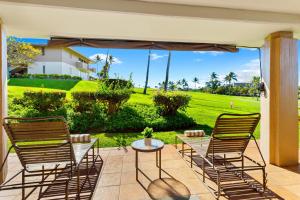 a patio with two chairs and a table with a view of a field at Maui's Newest 2 BR - California Coastal Inspired in Kaanapali