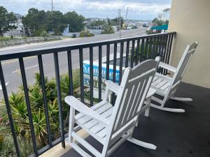 2 sillas blancas sentadas en un balcón con vistas a la calle en Summer Sands - 104 by Sea Scape Properties, en Wrightsville Beach