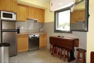 cocina con armarios de madera, mesa y nevera en Apartamentos Ababides Playa, en Baiona