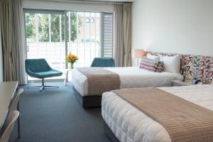 a hotel room with two beds and a chair and a window at Navigate Seaside Hotel & Apartments in Napier