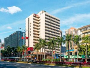 a tall white building on a city street with palm trees at Overseas Chinese Hotel in Zhuhai