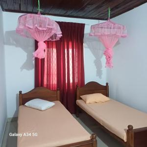 two beds in a room with pink curtains at Muthupalasa in Anuradhapura