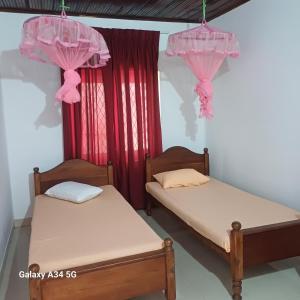 two beds in a room with pink curtains at Muthupalasa in Anuradhapura