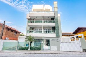 Un edificio blanco con una palmera delante. en Excelente ubicación a 200m de la playa de Bombinhas, en Bombinhas