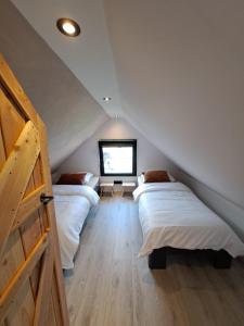 Un dormitorio abuhardillado con dos camas y una ventana. en Muziekskuur, en Hollum