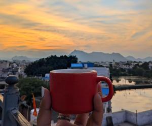 a person holding a red coffee cup in their hand at Whereabout Hostel Udaipur in Udaipur