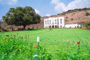 a large field of grass with a white house at The Serenity Resort Panchgani in Panchgani