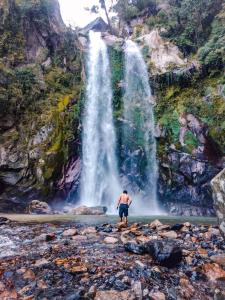 Un uomo in piedi di fronte a una cascata di bed and breakfast, also lunch and dinner if required a Mārkhu