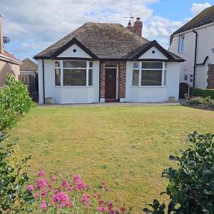a white house with a yard with pink flowers at Victoria Beach Cottage in Prestatyn