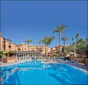 a large swimming pool in a resort with palm trees at Oasis Golf Apartment in Sitio de Calahonda