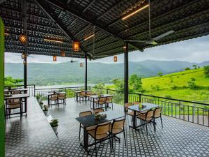 a restaurant with tables and chairs with mountains in the background at The Hosteller Panshet, Lakeview in Welhe