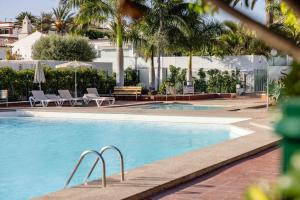 una piscina con tumbonas y palmeras en Deluxe Solycan - by Gestión Vacacional Canarias, en Maspalomas