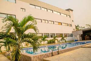 a building with a pool and palm trees in front of it at Hotel Etoile Du Stade in Yamoussoukro