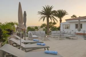 d'une terrasse avec des canapés, des parasols et des palmiers. dans l'établissement Villa Ginevra, à Arona