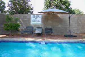 zwei Stühle und ein Sonnenschirm neben einem Swimmingpool in der Unterkunft Lulu Guest Lodge, Low-Density Suburbs, Victoria Falls in Victoriafälle