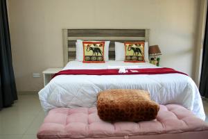 ein Schlafzimmer mit einem großen Bett mit einem rosa Ottomanen in der Unterkunft Lulu Guest Lodge, Low-Density Suburbs, Victoria Falls in Victoriafälle