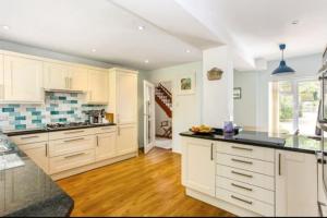 a large kitchen with white cabinets and a wooden floor at Delux 5 bed house lots private car parking, short walk to high st, shops in Fleet