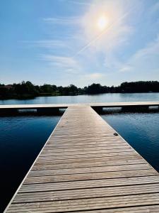 a wooden dock on a lake with the sun in the sky at Apartament WHITE GLOVE Deluxe Warmiński Port in Olsztyn