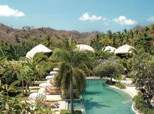 a resort swimming pool with umbrellas and a palm tree at Origin Lombok in Kuta Lombok