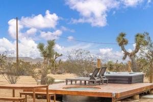 Una terraza con dos sillas y una mesa y algunas palmeras. en The Desert Serenity-Stunning views-Pool-Spa-BBQ, en Yucca Valley