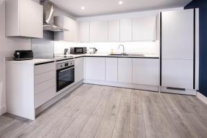 a kitchen with white cabinets and a wooden floor at Madison 2 Bedroom, 2 Bath Apartment in Hemel Hempstead